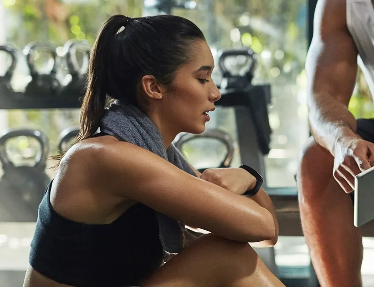 A woman resting after a workout while her trainer reviews her progress